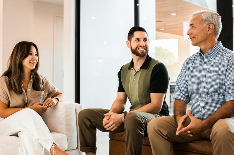 David Shapiro seated on a couch in conversation with a woman and an older man in a bright living room