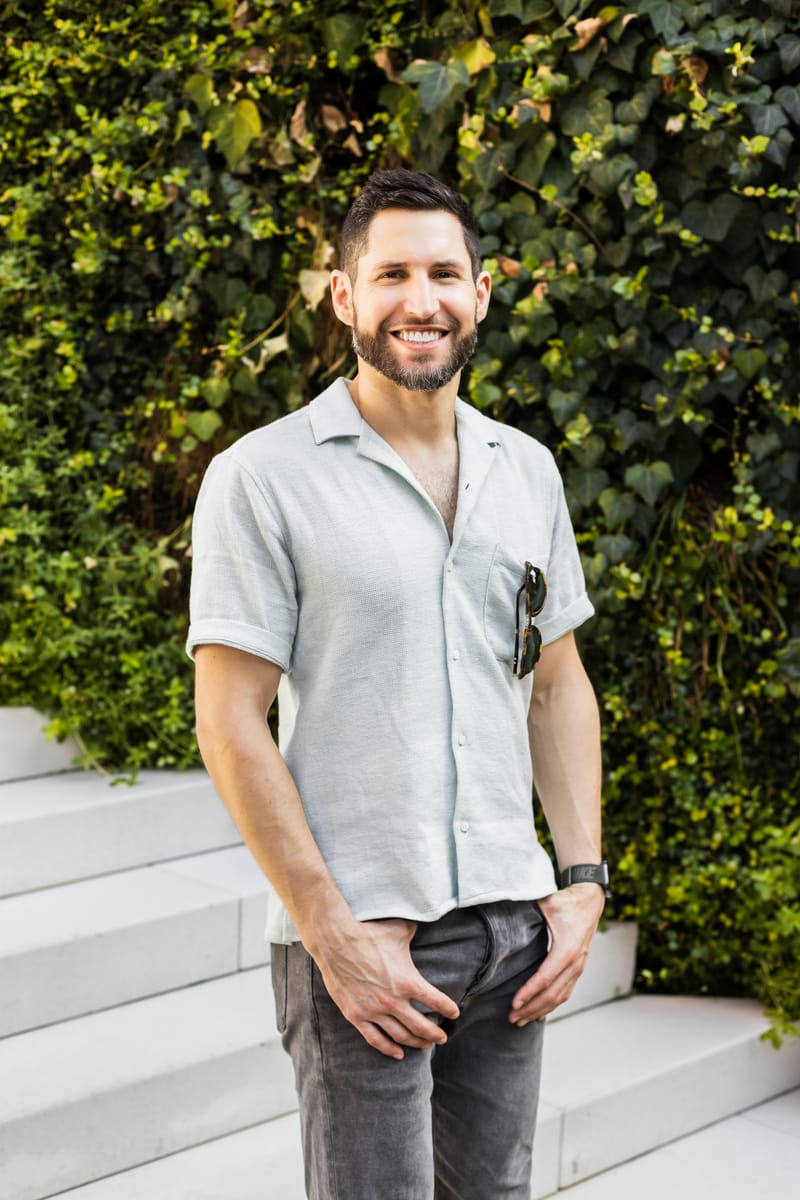 David Shapiro standing in front of an ivy-covered wall, smiling, sunglasses in his shirt pocket